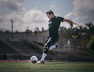 Athlete wearing the DonJoy Performance Bionic™ FullStop Knee Brace kicking a soccer ball