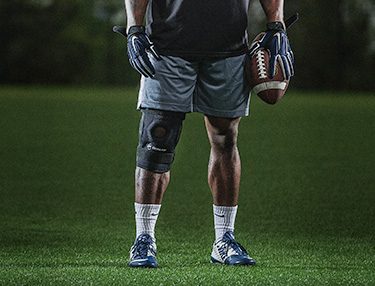 Athlete wearing the DonJoy Performance Bionic™ Knee Brace holding a football