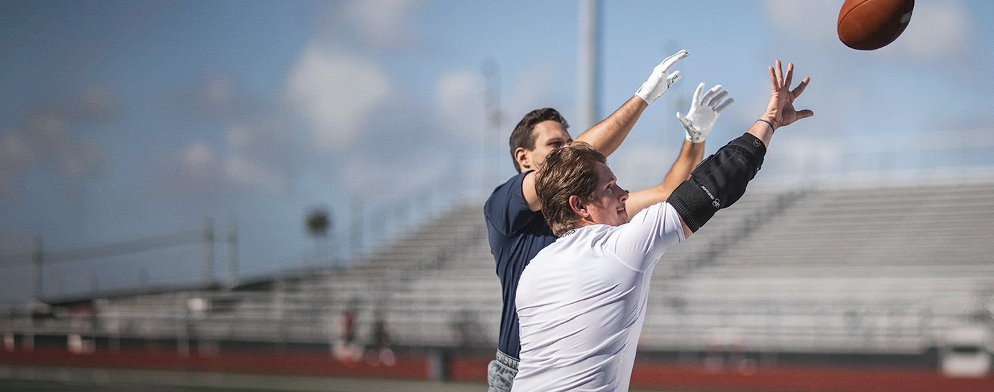 Athlete wearing the DonJoy Performance Bionic™ Elbow Brace playing football defending a receiver and attempting to knock the football away