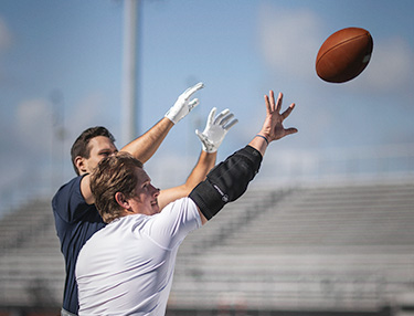 Athlete wearing the DonJoy Performance Bionic™ Elbow Brace playing football defending a receiver and attempting to knock the football away